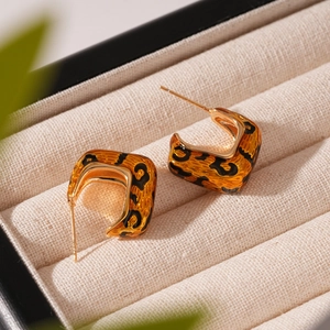 Macro shot of gold-plated leopard print U-shaped earrings on a beige velvet jewelry box