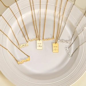 Detail of stainless steel Mama and MOM necklaces in gold and silver on ceramic tray