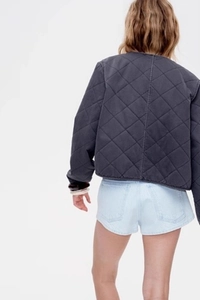Rear view of a dark grey quilted jacket with diamond patterns and light blue denim shorts