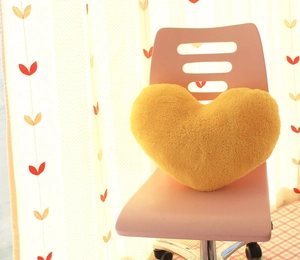 Close-up of a soft yellow heart-shaped plush pillow on a pink office chair