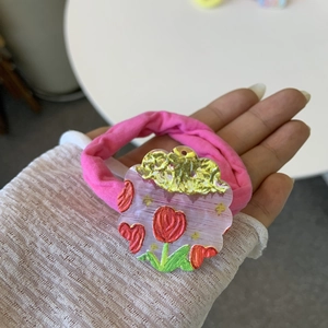 Detail of pink elastic hair tie featuring an acrylic piece with red tulip floral patterns