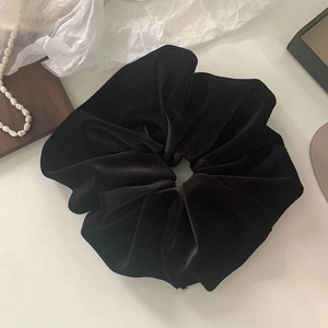 Detail of a large black velvet hair scrunchie with soft folds and elegant texture