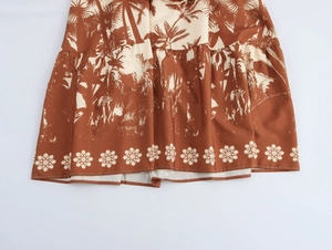 Close-up of brown maxi dress featuring cream palm tree prints and floral hem details