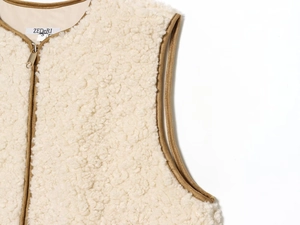 Detail of cream sherpa vest featuring a metal zipper and brown contrast piping trim