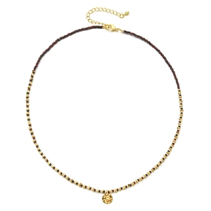 Macro shot of 18K gold-plated beads and textured pendant on a beaded necklace