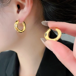 Close-up of chunky gold-plated hoop earrings featuring an inlaid zircon stone detail