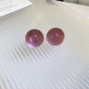 Macro shot of minimalist translucent purple resin sphere stud earrings on a textured surface