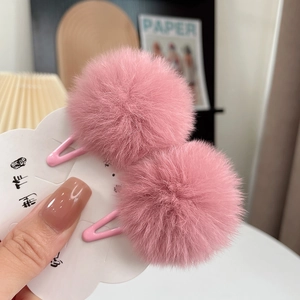 Close-up of two soft pink plush faux fur pom pom hair clips on a white cloud card display