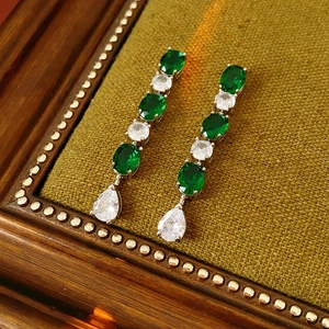 Détail de boucles d'oreilles avec pierres vertes et blanches sur fond de velours vert