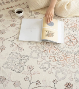 Close-up of a floral beige rug with a person reading a book and holding a coffee cup