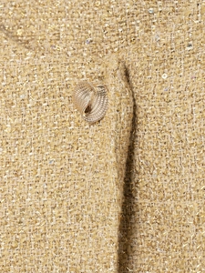 Detailed close-up of metallic tweed fabric texture with a unique gold metal button