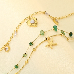 Gold layered anklet with heart pendant, green beads and starfish on silk background