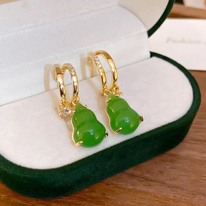 Close-up of golden gourd earrings with green glaze and pavé zircons on velvet