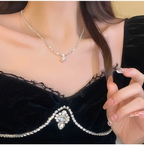 Close-up of a silver chain necklace with a lustrous white pearl pendant on a model