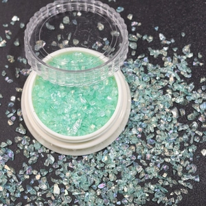 Macro shot of irregular green glitter flakes for nail art in a white plastic container