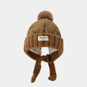 Detail of winter quilted trapper hat with fur pom-poms and Bonjour text label in brown