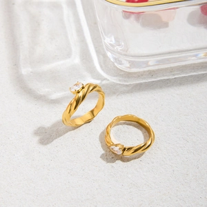 Detail of twisted gold titanium steel rings with oval zircon gemstones on a grey surface