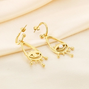 Detailed close-up of gold eye drop earrings with pearls on cream satin fabric