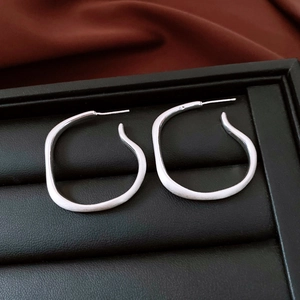 Detail of silver irregular fluid earrings on black leather texture jewelry box