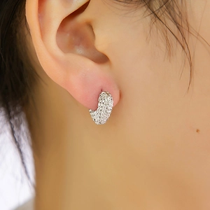 Détail d'une boucle d'oreille créole argentée texturée sur un mannequin avec motifs
