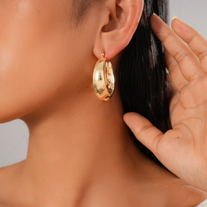 Close-up of minimalist gold pleated U-shape earrings worn by model on plain background