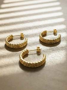 Macro detail of triple-layer textured C-shaped gold earrings on a wooden surface