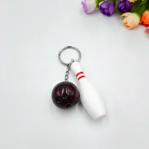 Miniature black bowling ball and pin keychain with metal ring on white background