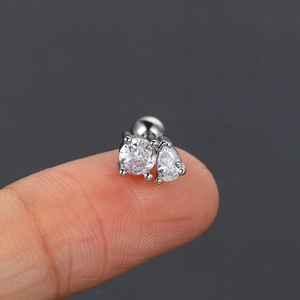 Macro shot of silver stud earring with round and pear-cut zircon stones on a fingertip