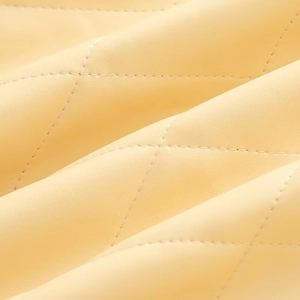 Dettaglio macro della trapuntatura a rombi e trama in pelle crema sul cappotto