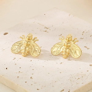 Detailed view of golden bee earrings placed on a beige textured stone surface