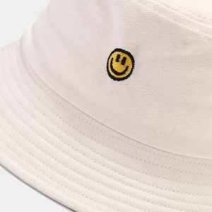 Close-up of a cream cotton bucket hat featuring a detailed yellow smiley face embroidery