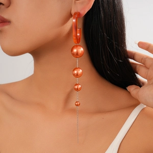 Detail of long orange acrylic drop earring with metallic spheres and silver chain fringe