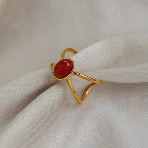 Detail of red oval gemstone ring with 18K gold-plated hollow band on beige fabric