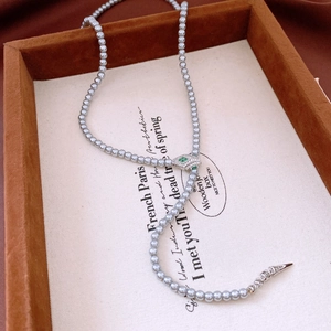 Macro detail of silver snake head clasp with green zircon eyes on grey pearl necklace