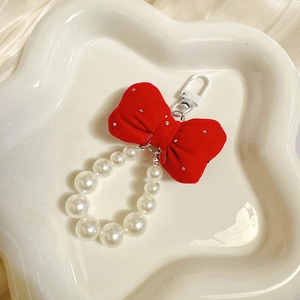Detail of red velvet bow and white pearl keychain displayed on a white ceramic plate