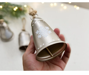 Detail der Metall-Weihnachtsglocke mit weißen Schneeflocken und rustikalem Hanfseil