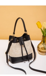 Detail of straw bucket bag with black leather frame, gold hardware, and drawstring closure