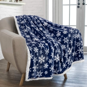 Navy blue flannel Sherpa blanket with white snowflake patterns on a modern grey sofa