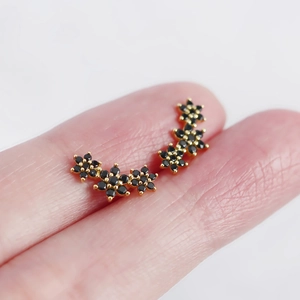 Macro view of gold flower earrings with black rhinestones held on fingers for detail