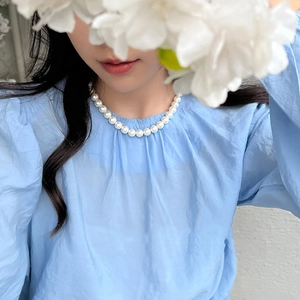 Close-up of elegant single-strand white pearl necklace worn on a model with a blue shirt