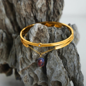 Vintage gold bangle with colorful natural stone pendant on a textured stone display