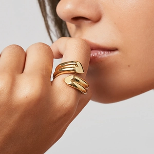 Nahaufnahme eines goldenen Doppelherz-Rings am Finger mit polierter Oberfläche