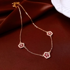Detailed view of rose gold flower pendant necklace with red crystals on brown velvet