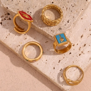 Detail of five 18K gold plated rings including red lip and palm tree motifs on stone