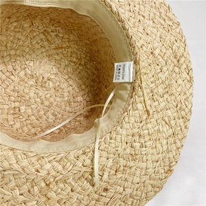 Macro detail of natural raffia straw hat showing inner weave and 100% material label