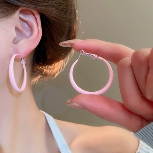 Close-up of pink round hoop earrings on ear and hand showing smooth matte finish