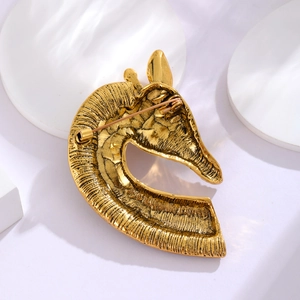 Golden horse head brooch with vintage texture and pin closure on white background