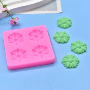 Pink silicone 4-cavity daisy flower mold with green DIY soap creations on blue background