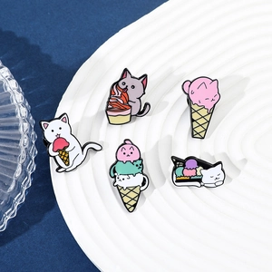 Detail view of five colorful enamel cat ice cream pins on a white ceramic plate