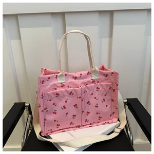 Detail of pink canvas tote bag with cherry print and dual front pockets on a chair